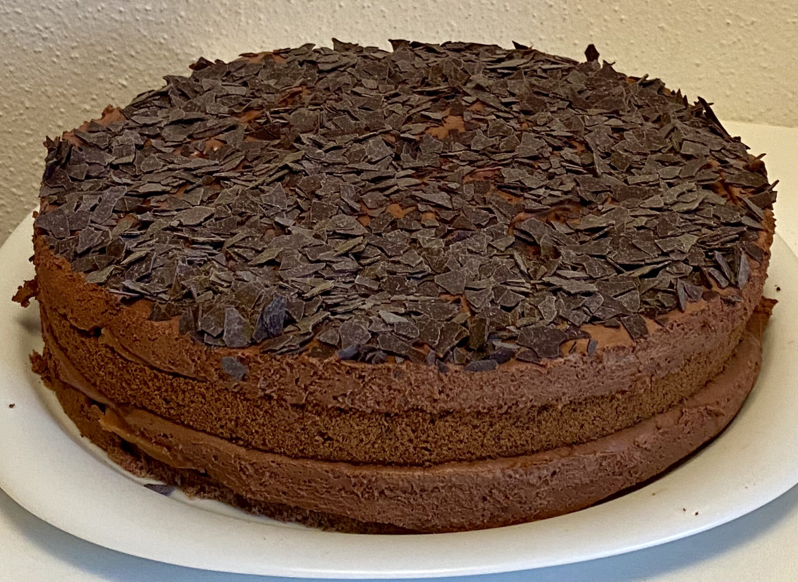 Eine Schokotorte als naked cake auf einem weißen Teller. Die Torte hat mehrere Schichten aus Biskuit und Schokocreme obendrauf sind Schokoraspeln.